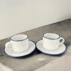 two white cups and saucers sitting on top of a stone counter next to each other