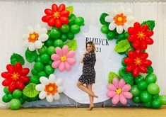 a woman standing in front of a backdrop with flowers and balloons