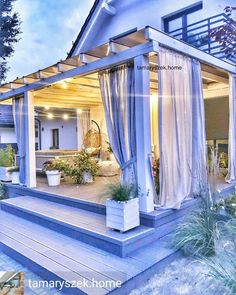 an outdoor living area is lit up with lights and curtains on the outside wall, along with potted plants