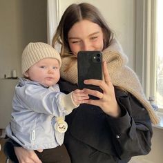 a woman holding a baby taking a selfie with her phone