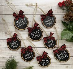 christmas ornaments with words and bows on them sitting next to pine cones, evergreen leaves and red berries