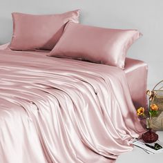 a bed with pink sheets and pillows on top of it, next to a basket full of flowers