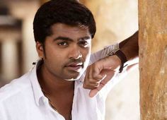 a man pointing at the camera while wearing a white shirt and brown bracelet on his wrist