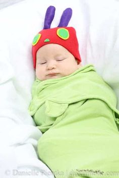 a sleeping baby wearing a red and green hat with purple ears on it's head