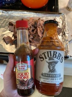 two bottles of barbecue sauce next to each other in front of an aluminum foil container