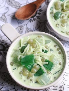 two bowls filled with noodles and vegetables on top of a floral table cloth next to a wooden spoon