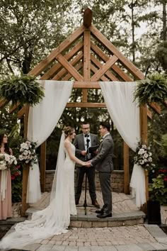 a bride and groom exchanging vows in front of an outdoor wedding ceremony arch with white drapes