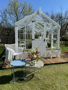 a small white greenhouse sitting on top of a grass covered field next to a table and chairs