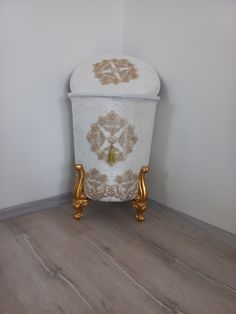 a white and gold trash can sitting on top of a wooden floor next to a wall