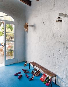 there are many pairs of shoes on the floor in front of an open window and a bench