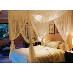 a white canopy bed sitting in a bedroom next to a window with curtains on it