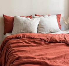 a bed with two pillows on top of it and an orange blanket in the middle