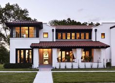 a large white house with lots of windows and lights on the front door is lit up at night