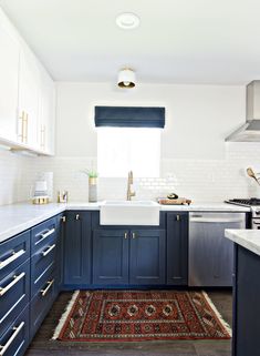 a kitchen with blue cabinets and rug in the middle, white counter tops on both sides