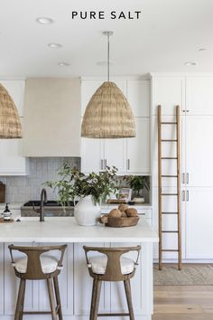 a kitchen with two hanging lights above the island and stools in front of it