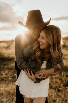 a man in a cowboy hat hugging a woman's back while the sun shines on her