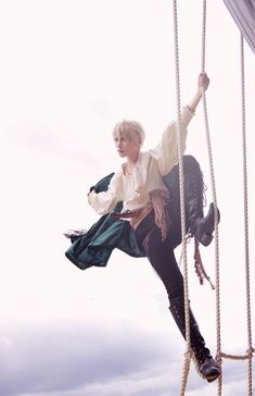 a woman in white shirt and black pants on a rope with her hand up to the side