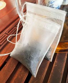 two bags of tea sitting on top of a wooden table next to a glass vase