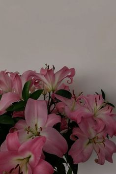 pink lilies in a vase on a white table top with green leaves and stems