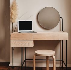 a laptop computer sitting on top of a wooden desk next to a mirror and stool