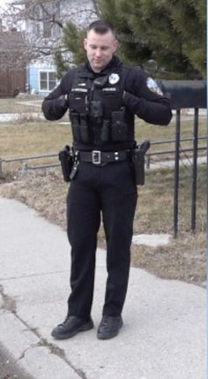 a police officer standing on the sidewalk in front of a fence with his hands behind his back