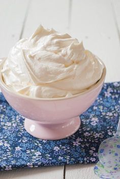 a pink bowl filled with whipped cream on top of a blue napkin next to a spoon