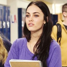 a woman holding a binder in her hand and looking at the camera with other people behind her