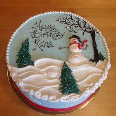 a frosted cake decorated with a snowman and trees