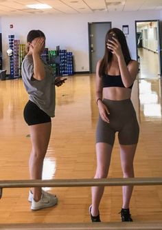 two people standing in a gym looking at their cell phones while one person covers his face with her hand