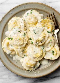 a white plate topped with ravioli covered in gravy next to a fork