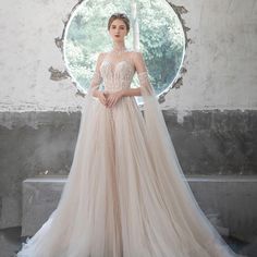 a woman standing in front of a round window wearing a wedding dress with long sleeves