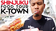 a man is eating a hot dog in front of a street with the words shinjuki food tour k - town