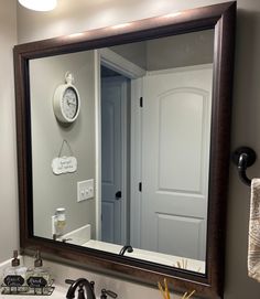 a bathroom sink with a mirror above it and a clock on the wall behind it