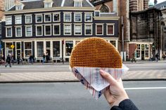 a person holding up a waffle sandwich in front of a building on the street