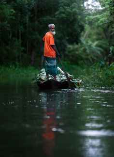 a man standing on top of a boat in the middle of a river surrounded by trees