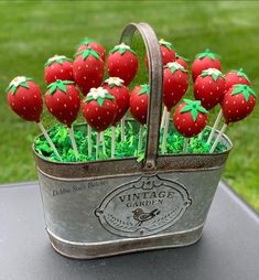 some strawberries are sitting in a metal basket on a table with grass and flowers