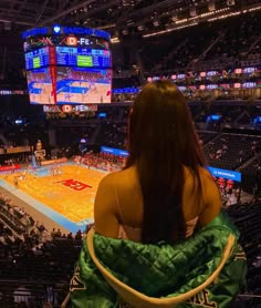 a woman sitting in a chair watching a basketball game on the big screen at an arena