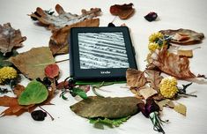 an electronic device surrounded by leaves and flowers on a white table with the screen turned off