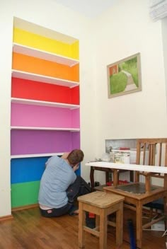 a man sitting on the floor in front of a book shelf with different colored shelves