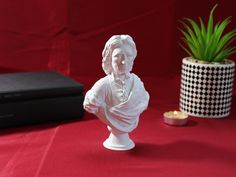 a white busturine sitting next to a potted plant on a red surface