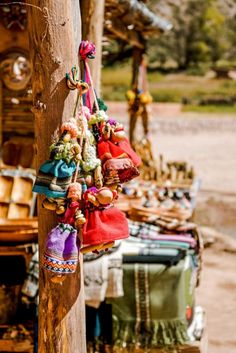 several colorful bags hanging from a wooden pole in front of other items on the ground