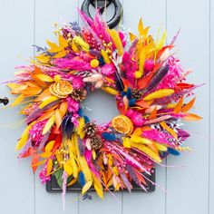 a colorful wreath hanging on the side of a white door with oranges, pinks and yellow feathers