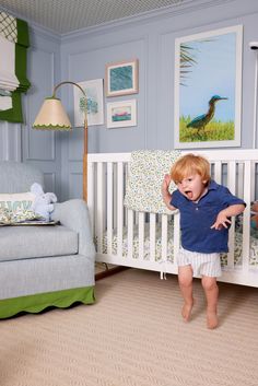 a little boy standing in front of a crib