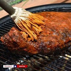 a large piece of meat is being grilled on a bbq grill with a brush