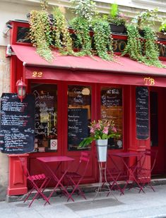 the outside of a restaurant with tables and chairs in front of it, covered by plants