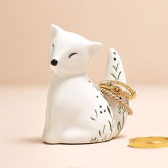 a small white fox figurine with a gold ring on it's back