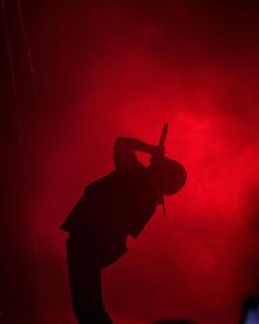 the silhouette of a person holding a microphone in front of a red light at a concert