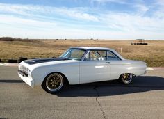 an old white car parked in a parking lot next to a grass covered field on a sunny day