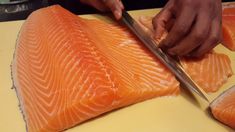 a person cutting up salmon on top of a yellow counter