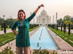 a woman standing in front of a fountain with her hand up to the sky and looking at the camera